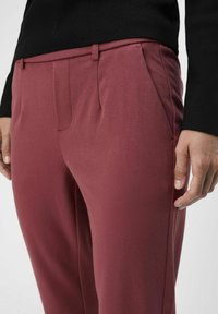 Bordowe spodnie o dopasowanym kroju, wykonane z gładkiego materiału, z bocznymi kieszeniami i slim fit, zestawione z czarnym dopasowanym swetrem.