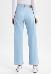Helle blaue weit geschnittene Jeans mit hoher Taille, ausgestattet mit einem Lederlabel auf der Rückseite und zwei Gesäßtaschen, kombiniert mit weißen Sneakern.