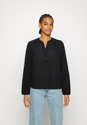 Blusa preta de manga longa com bolinhas brancas, apresentando um decote em V e detalhes de botões. Tecido suave e corte descontraído.