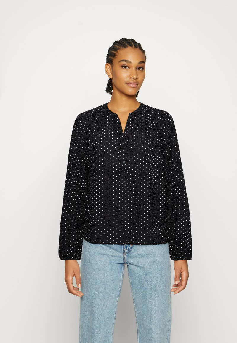 Blusa preta de manga longa com bolinhas brancas, apresentando um decote em V e detalhes de botões. Tecido suave e corte descontraído.