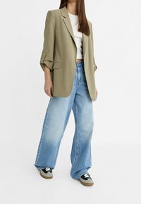 Överdimensionerad olivgrön blazer med uppvikta ärmar, matchad med vida ljusblå jeans och svarta sneakers. Slät tyg och avslappnad passform.