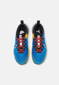 Scarpe da ginnastica blu e nere con tomaia in rete, accenti gialli a contrasto, lacci rossi e suole in gomma con un motivo testurizzato.