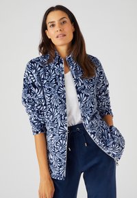 Giacca in pile blu navy con motivo floreale bianco, colletto alto, chiusura con zip e polsini a costine, abbinata a pantaloni blu scuro.