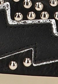 Cuero sintético negro con tachuelas plateadas y un patrón de costura en zigzag blanco en contraste. El primer plano revela la textura y los detalles del diseño.