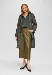 Zwart-wit houndstooth lange jas, groene satijnen knoopshirt, olijfgroene leren wijde broek en zwarte hoge hakken.