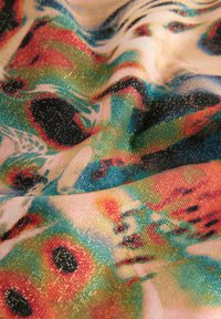 Tissu coloré et texturé avec une surface lisse et légèrement brillante. Présente un motif abstrait vibrant dans des teintes turquoise, rouge et noir.