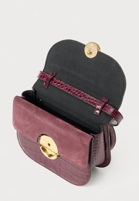 Borsa bordeaux con base lucida effetto coccodrillo e patta in morbida pelle scamosciata. Presenta una chiusura circolare dorata e una tasca interna con zip.