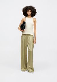 Haut sans manches beige clair associé à un pantalon large vert olive. Un sac à main noir lisse complète le look. Design simple et minimaliste.