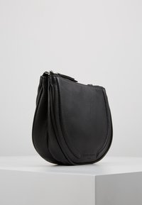 Borsa a sacchetto in pelle nera con una forma curva, superficie texture, chiusura con cerniera e un discreto marchio alla base.