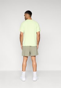 Ανοιχτό πράσινο βαμβακερό t-shirt με κανονική εφαρμογή, κοντά μανίκια, φορεμένο με μπεζ σορτς και λευκά αθλητικά παπούτσια. Απλό σχέδιο, χωρίς ορατά μοτίβα.