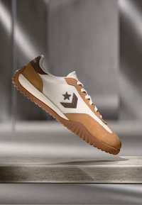 Balti ir rudi sportiniai bateliai su tekstūruota zomšos ir odos viršutine dalimi. Ypatumai: juodas žvaigždės logotipas, kreminės spalvos raišteliai ir ruda gumos padai.