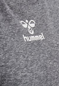 Bílý hummel logo se stylizovanou včelou na šedém texturovaném pozadí.