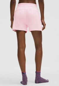 Rozā kokvilnas šorti ar elastīgu jostu, ar brīvu piegriezumu un nolocītām malām, apvienoti ar violetām un rozām teksturētām zeķēm.