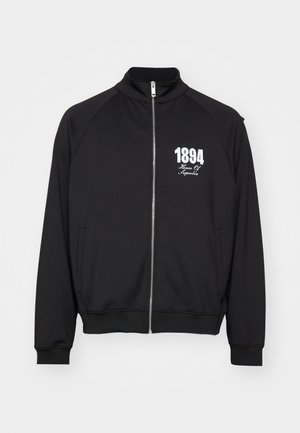 Svart treningsjakke med høy krage, hel glidelås og hvit trykt tekst "1894 House Of Superbia." Glatt stoff med ribbede mansjetter.