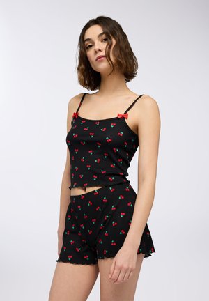 Completo in due pezzi nero a costine con motivi di ciliegie rosse, con spalline regolabili, fiocchi decorativi e bordi arricciati sui pantaloni corti.
