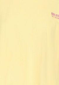Tissu jaune pâle avec un petit texte rose "SUN KISS" et des coordonnées en haut à droite.