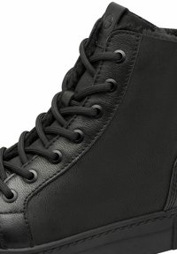 Black high-top sneaker made of textured leather, featuring round black laces and eyelets, with a flat rubber sole and minimalistic design.
