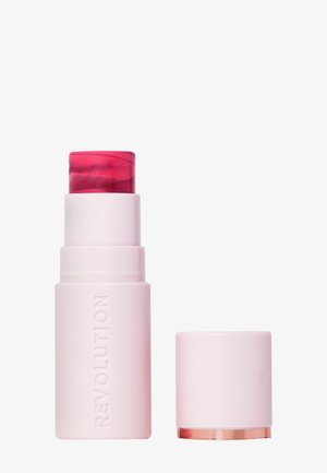Bâton de blush crème rose avec un sommet translucide rouge, de forme cylindrique, avec un texte gaufré "REVOLUTION" et un accent doré à la base.