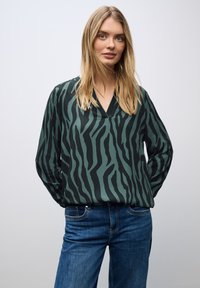 Blusa a maniche lunghe a righe zebrate verde e nera con scollatura a V, abbinata a jeans in denim blu. Tessuto morbido, vestibilità moderna.