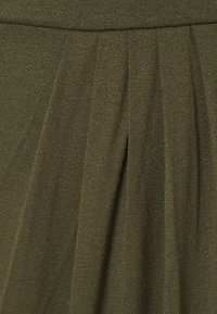 Jupe plissée vert olive en tissu tricoté texturé, dotée d'une ceinture et d'un drapé doux, mettant en avant des lignes verticales et un léger éclat.