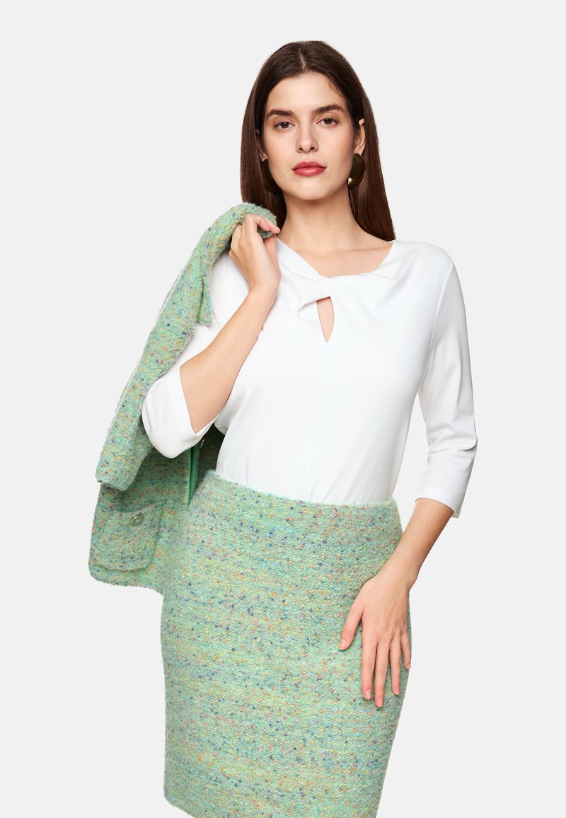 Weißes Oberteil mit einem Schlüsselloch-Detail, kombiniert mit einem mintgrünen strukturierten Rock und passendem Cardigan. Insgesamt ein abgestimmtes Zweiteiler-Outfit.