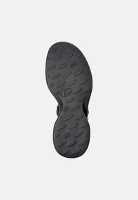 Czarna gumowa podeszwa buta z teksturowanym wzorem, w tym owalnymi i okrągłymi zagłębieniami, oraz wyraźnie widoczną etykietą rozmiaru "38".