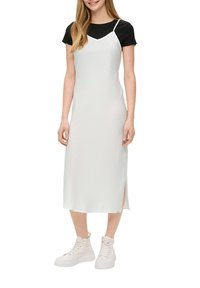 Robe blanche à bretelles spaghetti, en tissu texturé, avec une fente sur le côté, associée à un t-shirt noir et des baskets montantes blanches épaisses.