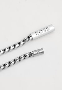 Twisted silver metal chain with cylindrical ends. One end features engraved "BOSS" and the other has a small circular fastening detail.