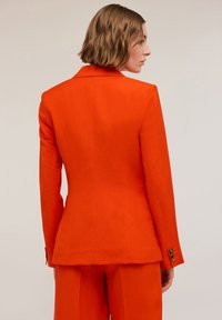 Orange kavaj med skräddarsydd passform, enkelknäppt design, snedskurna slag och knappade manschetter. Släta, strukturerade tyg.
