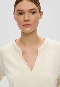 Lichtgekleurde top met een V-hals en ronde kraag, gemaakt van zachte stof. Kenmerkt subtiele stiksels en een ontspannen pasvorm.