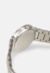Montre en acier inoxydable argenté avec un boîtier rond, une couronne texturée et un bracelet à maillons. Fini lisse et détails de design minimalistes.