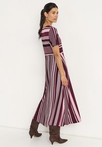 Maxikleid mit horizontalen und vertikalen Streifen in Burgunderrot, Pink und Weiß. Kurze Ärmel, fließender Stoff und ausgestellter Saum.