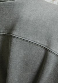 Sweat-shirt gris avec une texture côtelée, un col rond et un détail de couture visible le long de la couture de l'épaule.