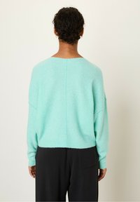Myntegrøn, struktureret sweater med lav skuldersøm og bred halsudskæring, parret med løstsiddende sorte bukser.