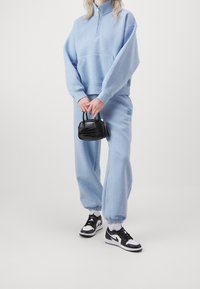 Hellblaues Fleece-Sweatshirt mit halbem Reißverschluss, kombiniert mit passenden Jogginghosen. Eine schwarze strukturierte Handtasche und schwarz-weiße Sneakers runden den Look ab.