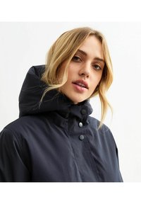 Marineblauwe gewatteerde jas met hoge kraag en oversized capuchon. Voorzien van zwarte drukknoopsluitingen en een gladde, matte textuur.