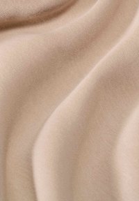 Tessuto beige con una superficie liscia e leggermente texturizzata, caratterizzata da onde e pieghe sottili che creano ombre delicate.