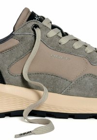 Primo piano di una sneaker in suede grigia e beige con suola in gomma, lacci beige e logo "HOFF" sul lato e sulla punta dei lacci.