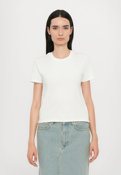 T-shirt en coton blanc à manches courtes avec un col rond, associé à une jupe en denim bleu clair présentant des coutures visibles et une silhouette droite.