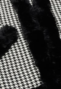 Accente de blană sintetică neagră pe un fundal cu model houndstooth în alb și negru, având o finisare moale și texturată.