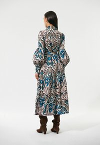 Langes, floral gemustertes Kleid mit Puffärmeln, tailliertem Schnitt und gestuftem Rock in den Farben Blau, Pink und Beige. Getragen mit braunen, kniehohen Stiefeln.