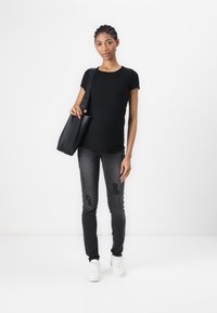 Top negro de manga corta con acanalado, jeans gris ajustados con acentos desgastados y zapatillas blancas. La modelo sostiene un gran bolso negro de hombro.