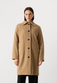 Manteau en laine beige avec un col, comportant des boutons marron et des poches latérales, présenté dans un design droit. Texture lisse, peu de détails.