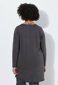 Langärmliges, dunkelgraues Hemd mit bequemer Passform. Der Stoff wirkt weich mit einer dezenten, gebrauchten Textur und abgerundetem Saum.