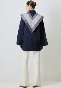 Cămașă de marina cu un guler V larg din satin gri, mâneci clopot și un croi lejer, asociată cu pantaloni albi evazați și pantofi negri.