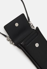 Czarna torebka typu crossbody o gładkiej, skórzanej teksturze, zapinana na zatrzask, z ozdobami w postaci łańcuszka i przegródkami na karty wewnątrz. Zwarta, prostokątna forma.