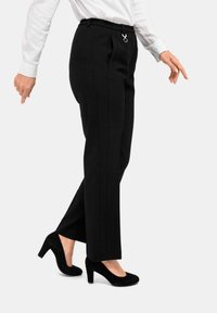 Zwarte op maat gemaakte broek met een hoge elastische tailleband en een zilveren accentring, gecombineerd met zwarte hoge hakken en een witte long-sleeve top.