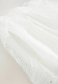 Îmbrăcăminte albă cu detalii elaborate din dantelă, textură moale și un design fluid cu modele subtile de broderie pe întregul material.