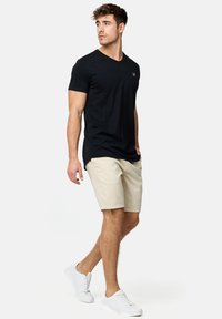 Sort V-hals t-shirt, beige shorts, hvide sneakers. Casual pasform, korte ærmer, glat bomuldsstof, minimal branding på skjorten.