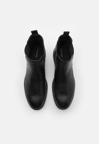 Bottines en cuir noir avec panneaux latéraux élastiques et languettes pour enfiler. Texture lisse avec coutures le long de la semelle, design minimaliste.